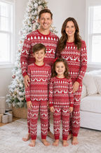 Family standing beside a snowy Christmas tree in matching red pajamas with white Fair Isle reindeer and tree patterns.