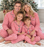 Family cuddling on a blanket beside a Christmas tree in red and white striped button-up pajamas with green trim.