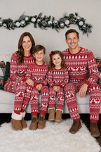 Family sitting on a sofa beneath a garland in matching red and white Fair Isle Christmas pajamas and winter boots.