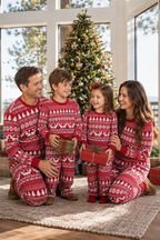 Family sitting on a rug holding gifts in red and white Fair Isle Christmas pajamas beside a decorated tree.