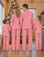 Back view of a family in red and white vertical-striped pajamas facing a Christmas tree in a wooden cabin.