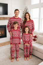 Family standing in a bright living room in red and white Fair Isle Christmas pajamas, with a tree and fireplace behind.