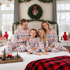Family of four sitting on a bed beneath a Christmas wreath in matching Fair Isle holiday pajamas.