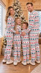 Family of four standing beside a decorated Christmas tree in matching reindeer and snowflake pajama sets.