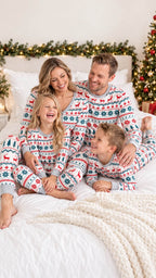 Parents and two children relaxing on a bed in matching red, green and white Fair Isle Christmas pajamas.