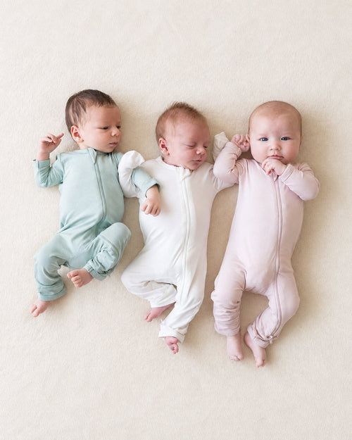 Three babies wearing mint, white and pink footless zip rompers
