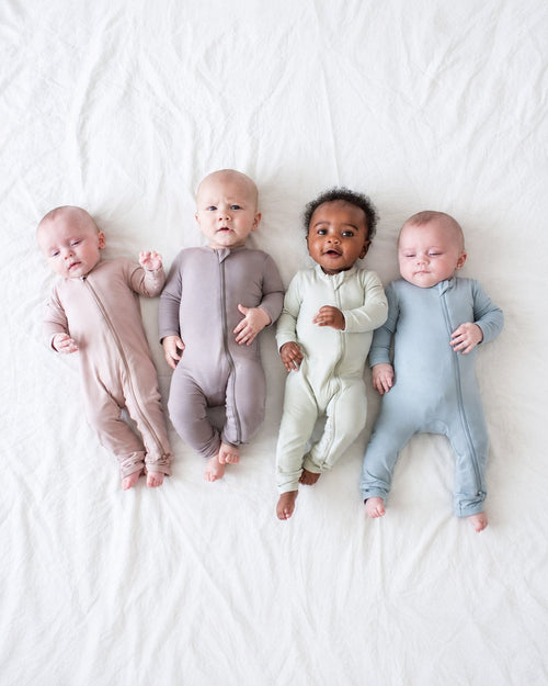 Four babies wearing pastel long-sleeve zip-front rompers with open feet