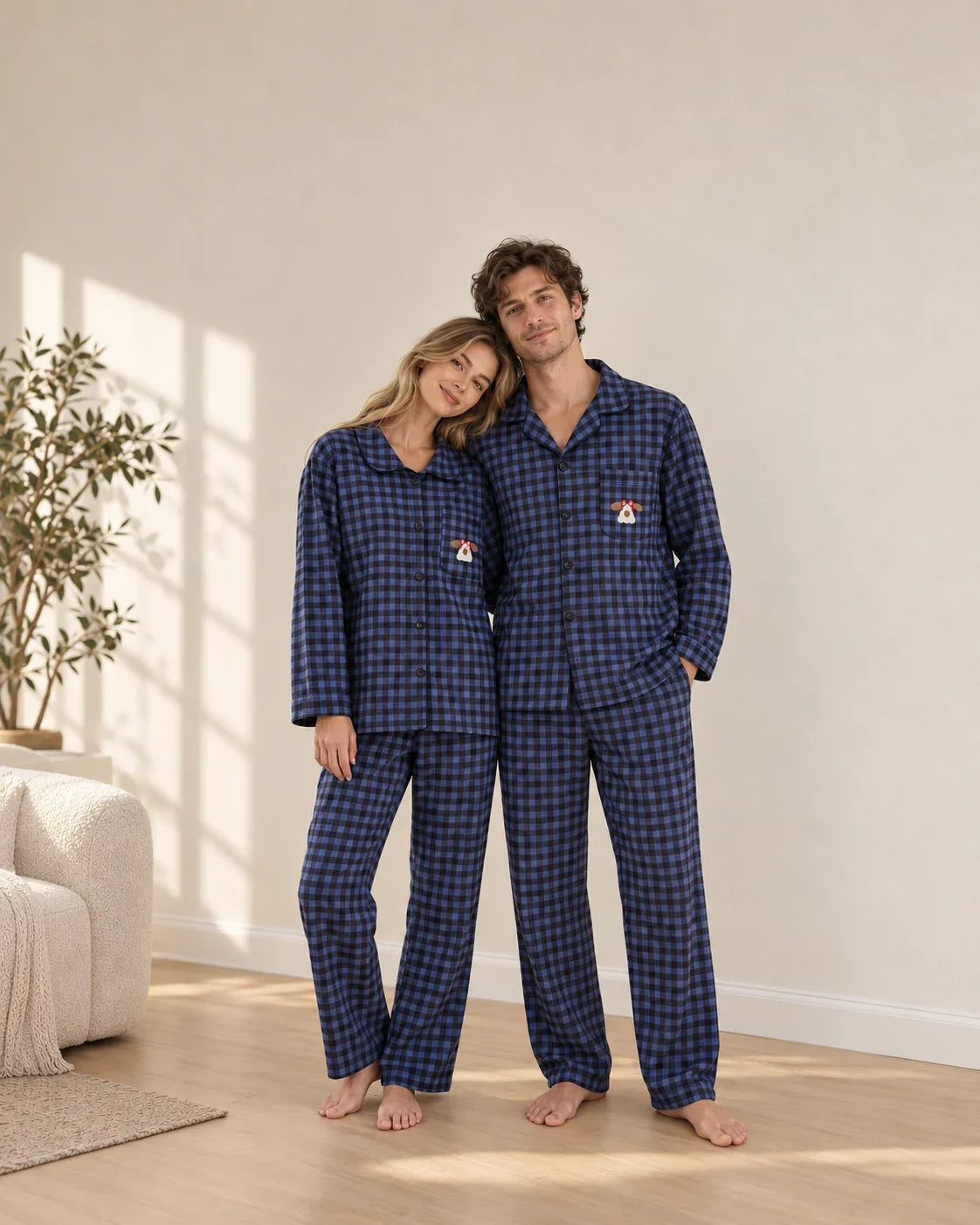 Couple standing in matching blue and black plaid pajamas with embroidered dog chest pockets, long sleeves and full-length pants.