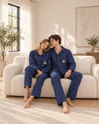 Couple relaxing on a cream sofa in blue plaid pajamas with black buttons and embroidered dog chest pockets.