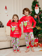 Two children wearing red Grinch tops and light gray printed Christmas pajama pants beside a tree