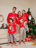 Family wearing red Grinch tops and light-colored character-print pajama pants beside a Christmas tree