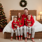 Family wearing red Grinch tops and light gray printed pajama pants beside a decorated bed and Christmas tree