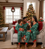 Family sitting on a living room sofa in matching green Fair Isle Christmas pajamas beside a glowing decorated Christmas tree.