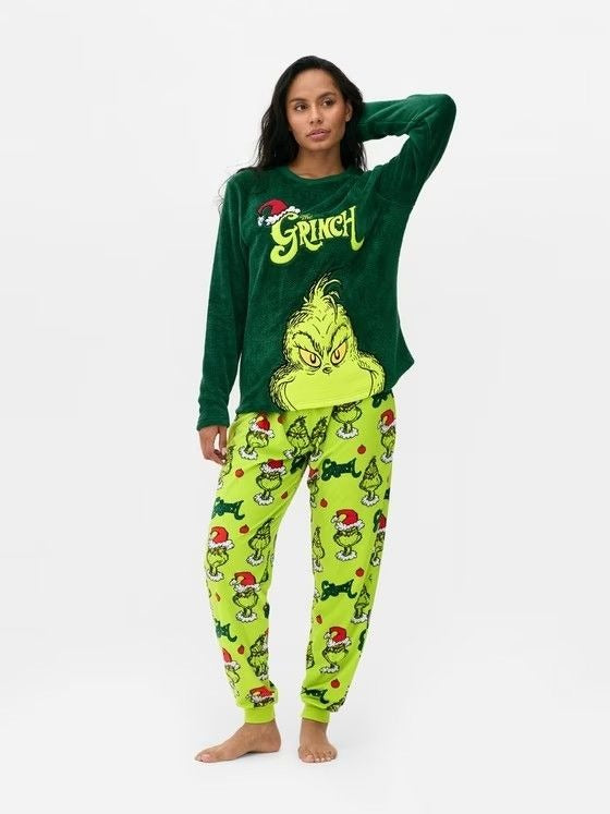 Woman posing with raised arms in a dark green Grinch top and lime-green printed pajama pants