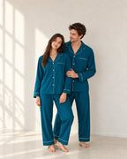 Standing portrait of a couple in deep sea blue pajamas, showing notched collars, pale buttons and thin white piping on the chest pocket tops.