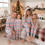 Family of four seated together in a decorated holiday living room wearing matching reindeer and snowflake pajamas.