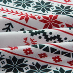 Extreme close-up of soft ribbed pajama fabric showing detailed red and green Fair Isle pattern with snowflakes, reindeer, and pine trees on a white background.
