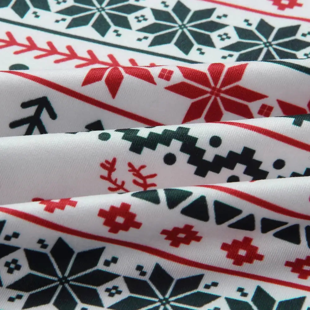 Extreme close-up of soft ribbed pajama fabric showing detailed red and green Fair Isle pattern with snowflakes, reindeer, and pine trees on a white background.
