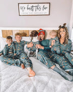 Family of five with their pet dog sitting together on a white bed wearing matching dark green safari animal printed Christmas pajamas.