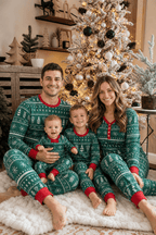 Family sitting beside a lit Christmas tree in forest green pajamas with white Fair Isle patterns and red cuffs.