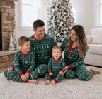 Family on a rug beside a stone fireplace in green Christmas pajamas with white tree and snowflake patterns.