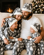 Parents cuddling two children in grey tree-print Christmas pajamas and matching hats, with dad in a white T-shirt.