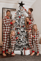 Family decorating a snowy Christmas tree in matching red, white and black plaid pajamas with red cuffs.