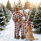 Family with three kids and a Golden Retriever wearing matching red and cream plaid holiday pajamas at an outdoor snow-covered Christmas tree farm with a wooden sled.
