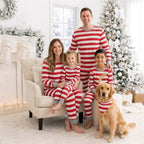 Family in red and white striped Christmas pajamas beside a tree, with a dog wearing a matching striped bandana.