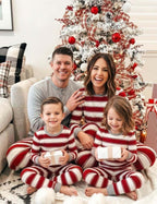 Parents and two children holding gifts beside a Christmas tree in red and white striped pajamas, dad in grey.