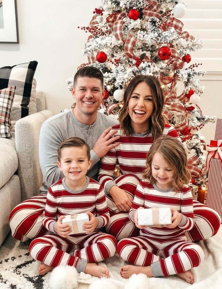 Parents and two children holding gifts beside a Christmas tree in red and white striped pajamas, dad in grey.