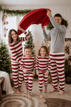 Parents holding a red blanket over two children in coordinated red and white striped Christmas pajamas.