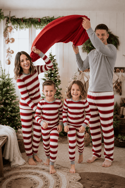 Parents holding a red blanket over two children in coordinated red and white striped Christmas pajamas.