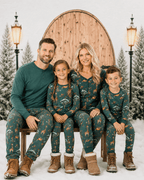 Family sitting on a bench in teal animal-print Christmas pajamas and boots against a snowy doorway backdrop.