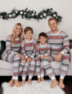 Family sitting on a sofa beneath a holiday garland in grey Christmas pajamas with red reindeer and green trees.