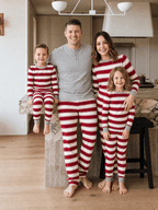 Family in red and white striped Christmas pajamas in a kitchen, with dad wearing a grey Henley top.