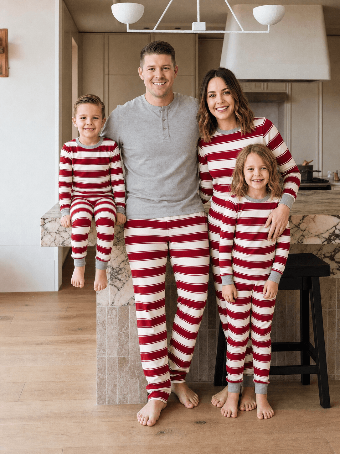 Family in red and white striped Christmas pajamas in a kitchen, with dad wearing a grey Henley top.