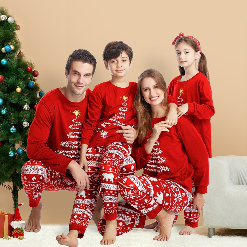 Family of four sitting by a decorated Christmas tree in matching red holiday pajamas featuring white brush-stroke Christmas tree tops with yellow stars and Nordic Fair Isle polar bear print pants.