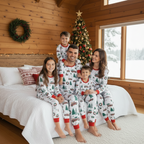 Family of five sitting on a bed in a rustic cabin wearing matching white Christmas pajamas with vintage red truck patterns.