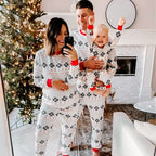 Full family mirror selfie with mom, dad, and baby wearing matching white snowflake holiday pajamas.