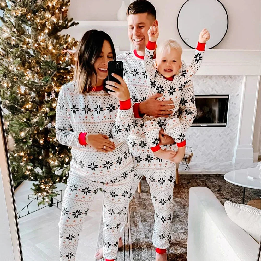 Full family mirror selfie with mom, dad, and baby wearing matching white snowflake holiday pajamas.