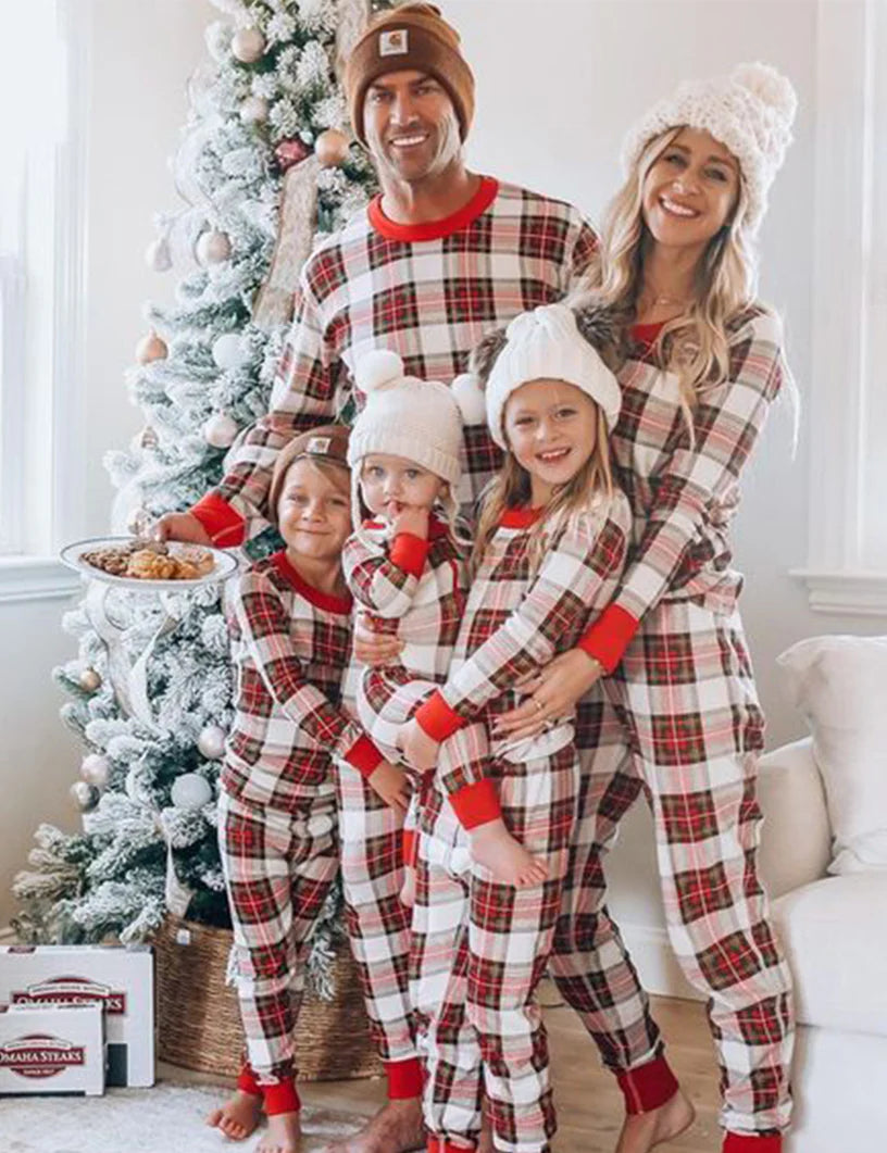 Family of five wearing matching cream and red plaid Christmas pajamas with red cuffs, standing together in front of a white frosted Christmas tree.