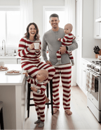 Mom and dad enjoying coffee and cookies with kids in a white kitchen wearing matching red and white striped Christmas pajamas.