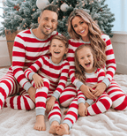 Parents and two children laughing by a Christmas tree in pajamas with wide red and white stripes and grey trim.