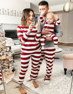 Parents and baby taking a mirror selfie wearing matching red and white candy cane striped Christmas pajamas with grey cuffs near a festive tree.