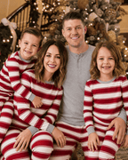 Family portrait beside a Christmas tree in red and white striped pajamas, with dad in a grey top.