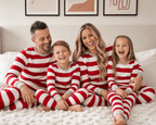 Family sitting together on a bed in matching Christmas pajamas with wide red and white stripes and grey cuffs.