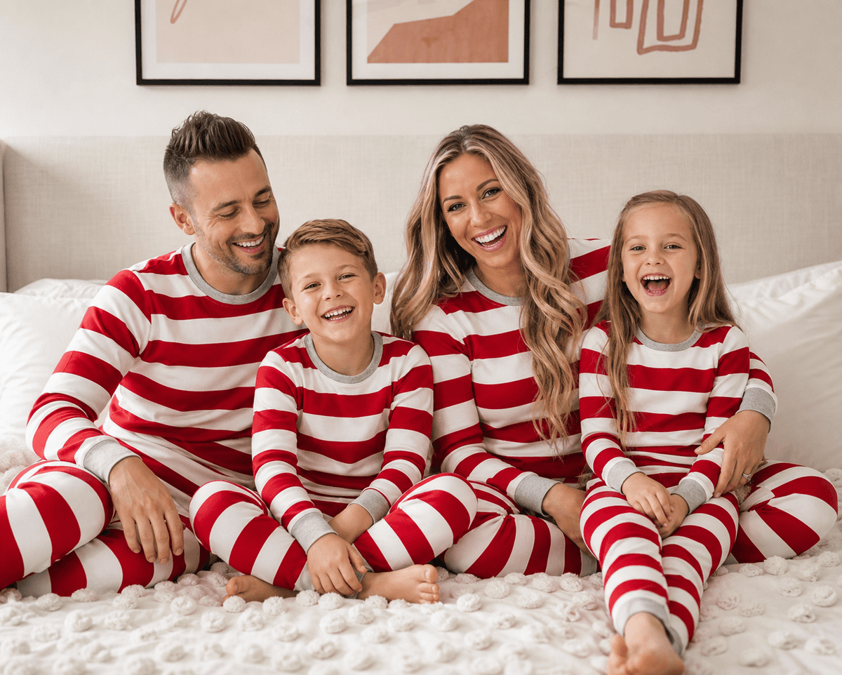 Family sitting together on a bed in matching Christmas pajamas with wide red and white stripes and grey cuffs.