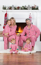 A family of five sitting in front of a warm lit fireplace wearing matching red and white candy cane striped holiday pajamas.