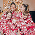 Family of five with three kids smiling together in front of a decorated Christmas tree, all dressed in matching long-sleeve red and white Fair Isle holiday pajama sets.